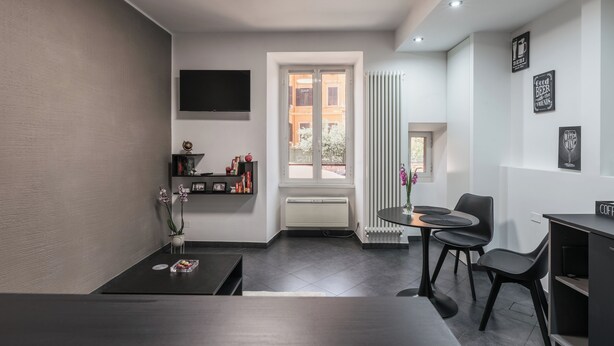 Una sala de estar moderna con un sofá oscuro, una mesita y una mesa de centro. Se ve una ventana con vistas a edificios.