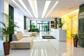 A modern lobby with a reception desk, seating area, and potted plants.
