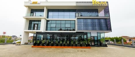 A modern hotel with a glass facade, a visible Hertz sign, and a well-maintained outdoor area with potted plants.