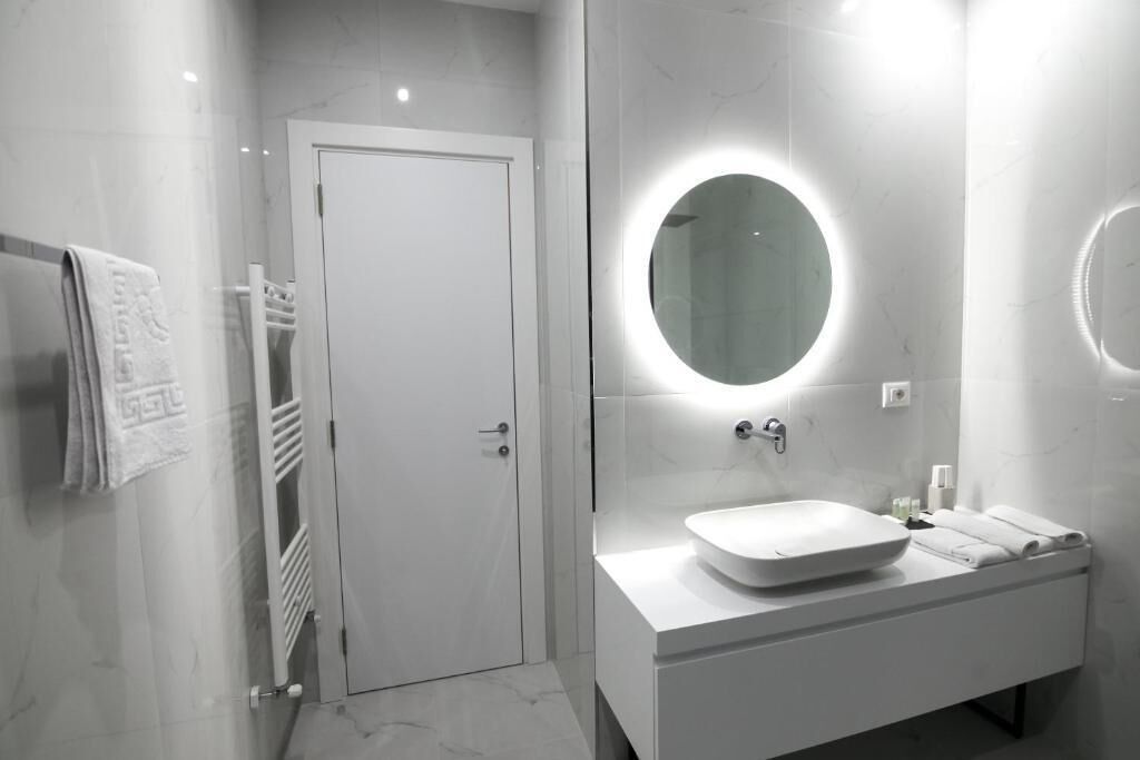 Een moderne badkamer met een witte wastafel, een ronde spiegel en een deur.