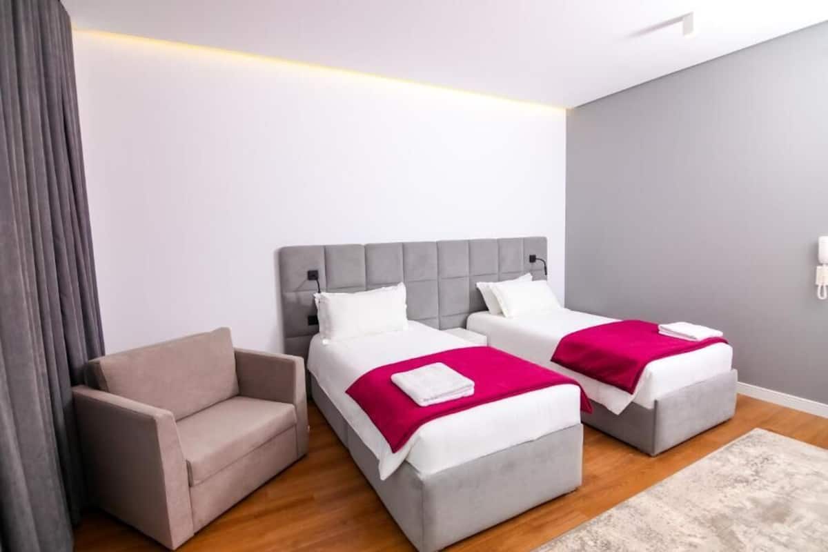 A hotel room with two beds, a sofa, and a phone on the wall.