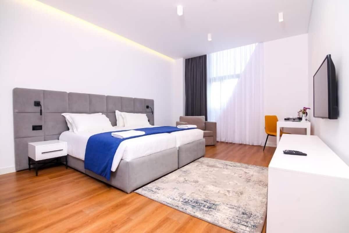 A modern hotel room with a large bed, a desk, and a TV.