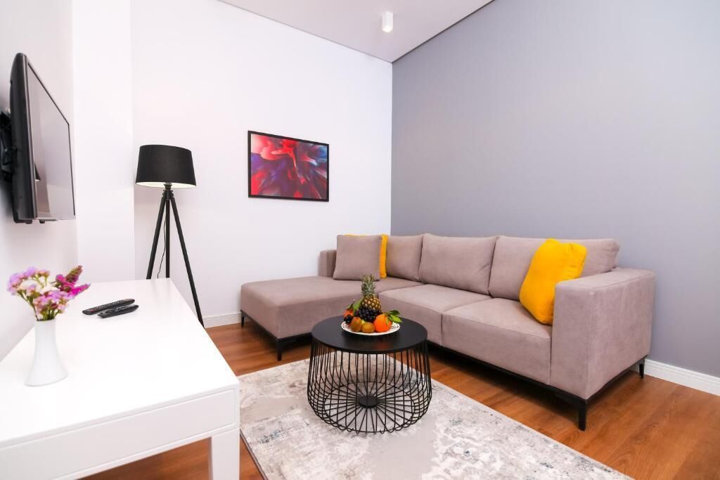 Ein modernes Wohnzimmer mit einem weißen Fernsehschrank, einer schwarzen Stehlampe, einem grauen Sofa mit gelbem Kissen und einem runden Couchtisch mit Obst.