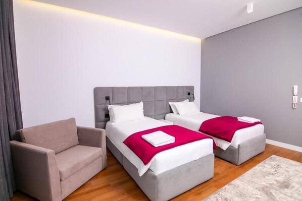 A modern hotel room with two beds, a sofa, and a wooden floor.