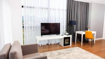 Ein modernes Wohnzimmer mit einem Flachbildfernseher auf einem weißen Konsolentisch, einer Couch, einem kleinen Tisch mit Lampe und einem Sessel.