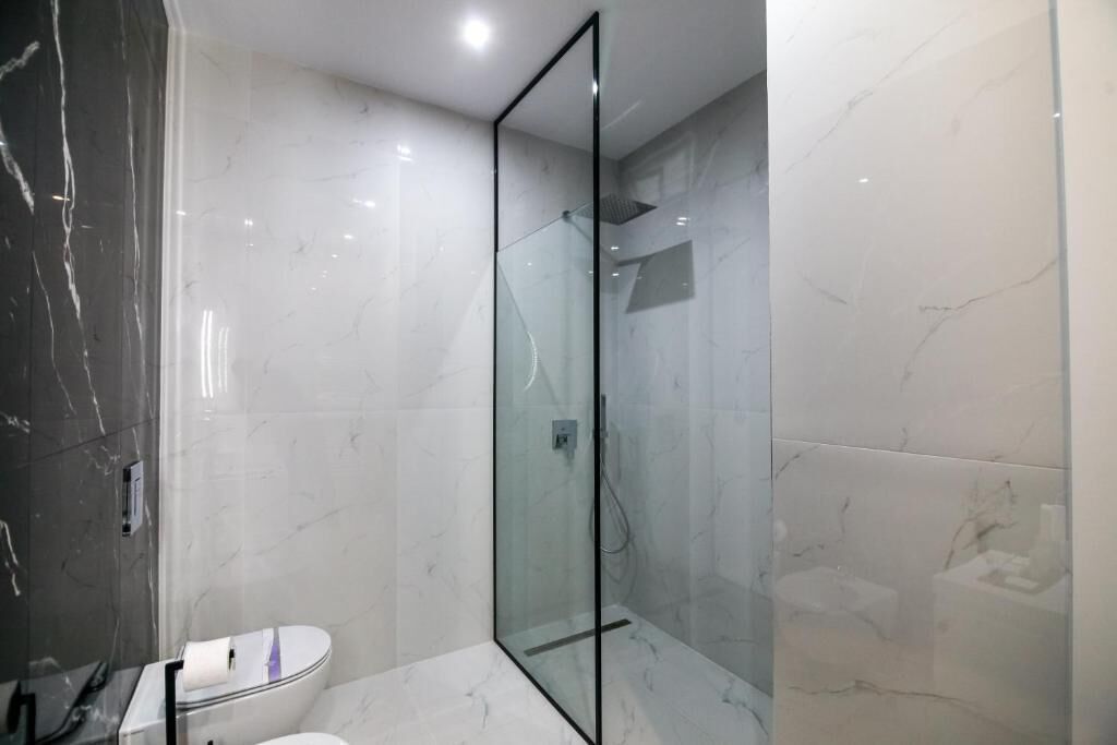 Un baño moderno con ducha envuelta en vidrio, inodoro y suelo de mármol.