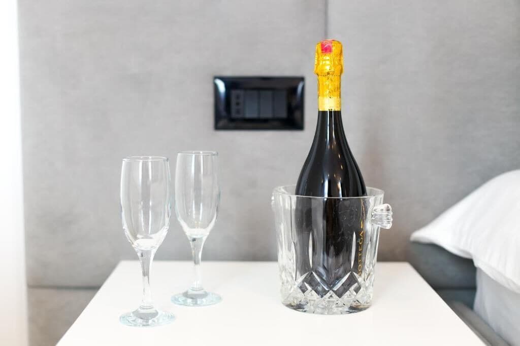 Une bouteille de champagne dans un seau à glace transparent, posée sur une table blanche, avec deux verres vides à côté.