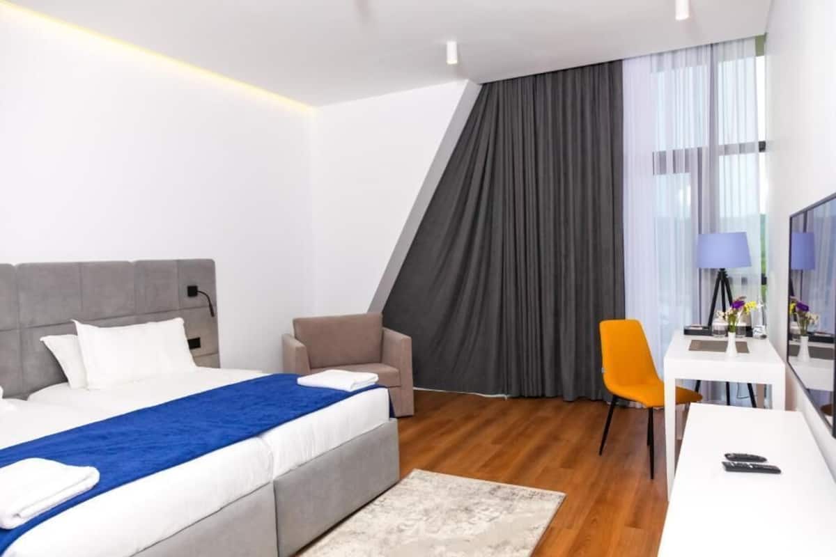A modern hotel room with a bed, a desk, a chair, and a TV.
