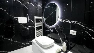 Un baño moderno con una pared de mármol negro, un lavabo blanco, un espejo y un perchero.