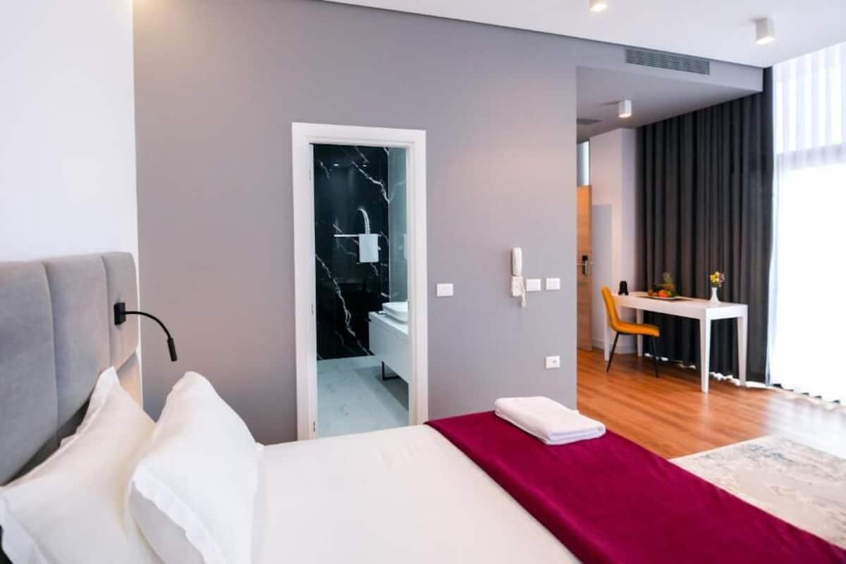 A modern hotel room with a bed, a desk, and a bathroom visible through an open door.