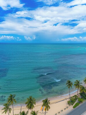 A beach with clear turquoise waters, palm trees, and a road leading to the beach.