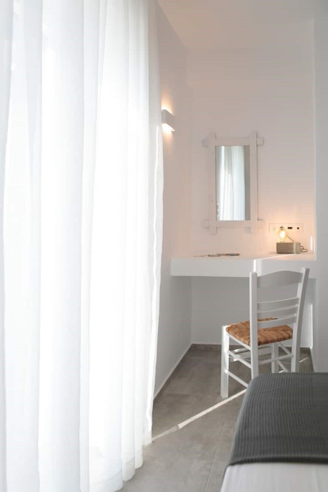 Une petite pièce blanche, avec un bureau, une chaise et un lit.