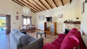 A living room with a sofa, a red armchair, a TV on a wooden cabinet, and a fireplace. - Finca Macías (Cártama)