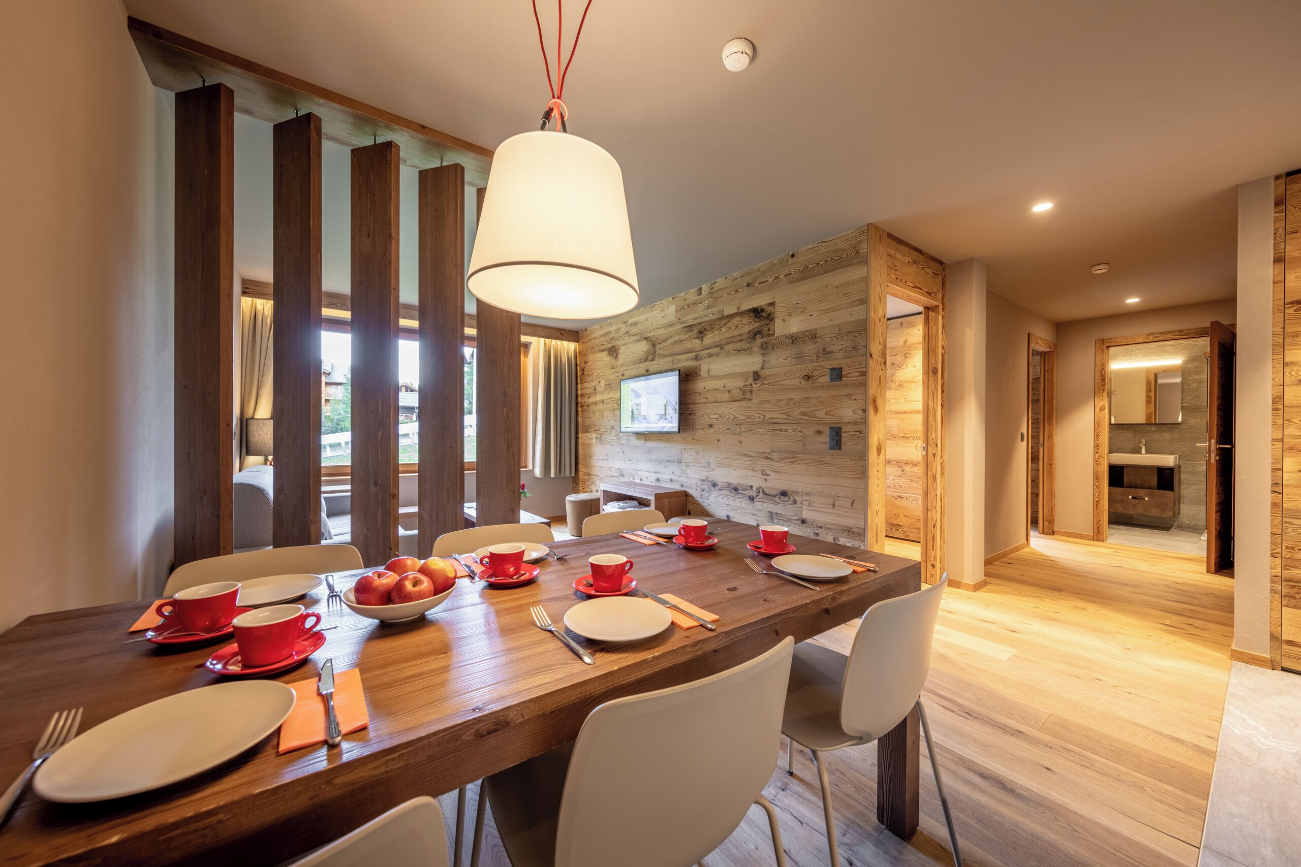 Un comedor con una mesa de madera dispuesta para cuatro personas, sillas y una lámpara colgante.
