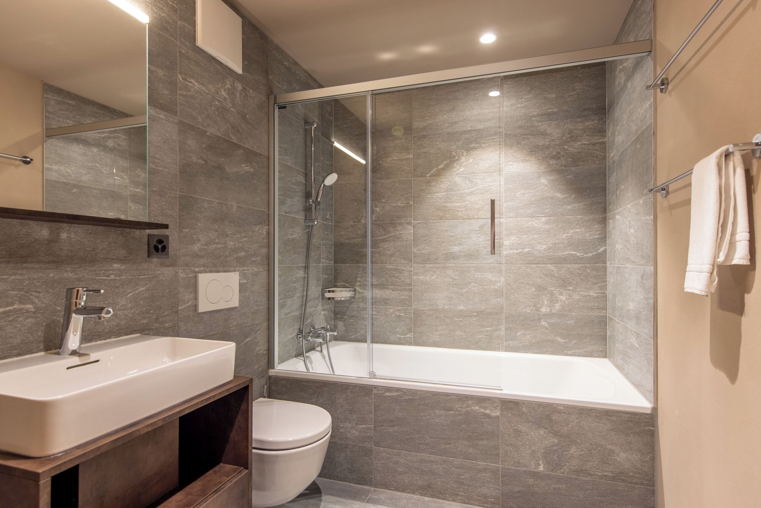 A modern bathroom with a glass-enclosed shower, a white sink, and a toilet.