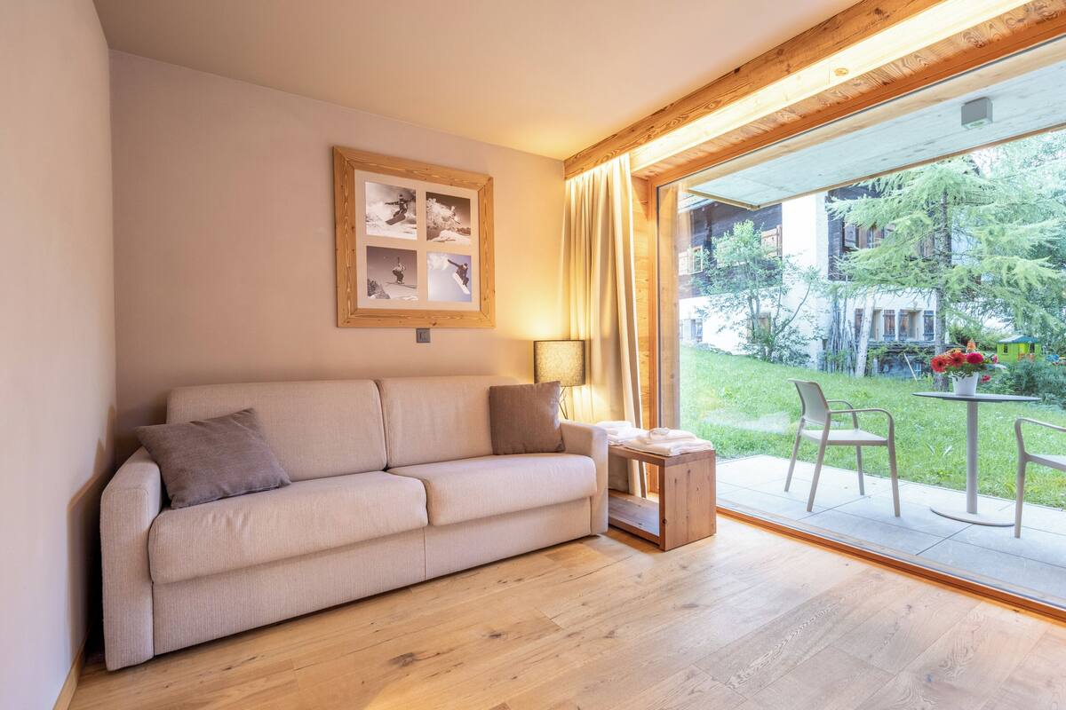 A living room with a sofa, a small table, a lamp, and a glass door leading to an outdoor area with chairs and a table.