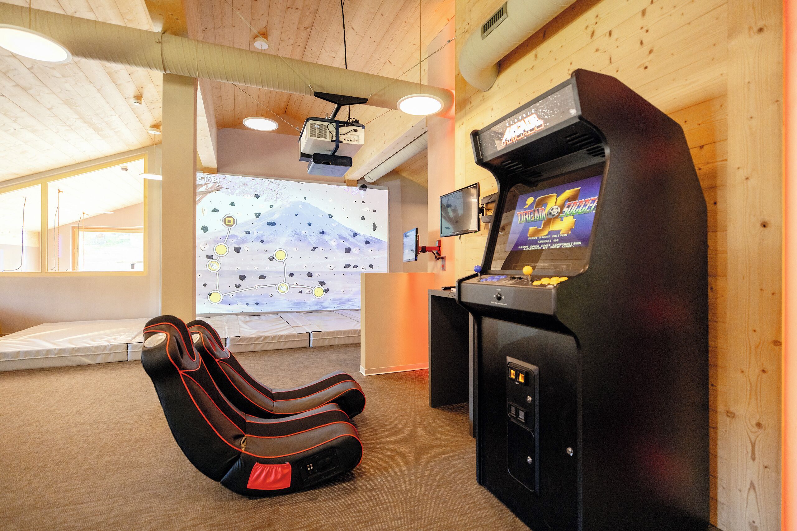 Una habitación con consola de videojuegos, pantalla de proyección, sillón reclinable y techo de madera.