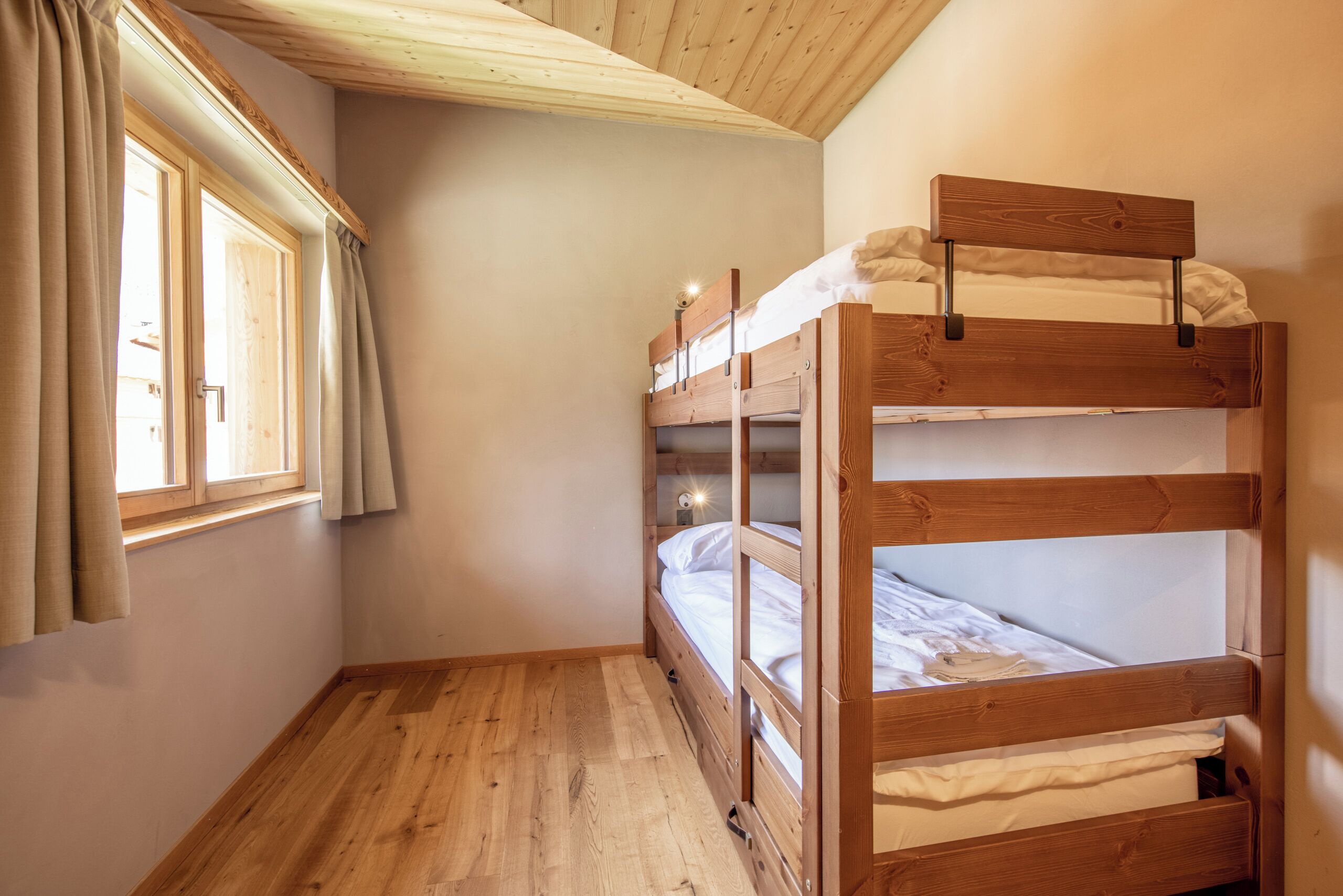 Ein Zimmer mit einem Holzbett, einem Fenster mit Vorhängen und Holzboden.