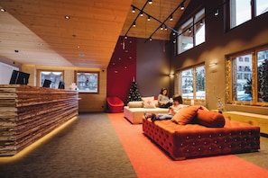 A modern interior with a wooden ceiling, large windows, a red sofa, a Christmas tree, and a stack of books. - SWISSPEAK Resorts by Pierre & Vacances Premium Zinal (Anniviers)