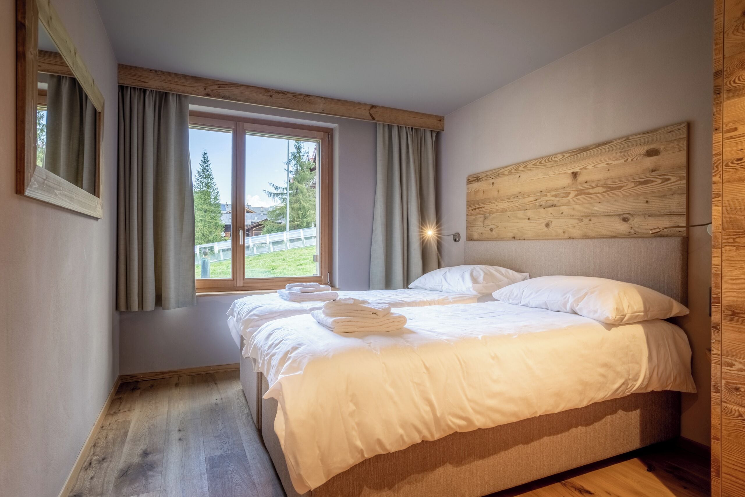 A bedroom with a bed, a window with curtains, a wooden headboard, and a view of trees outside.