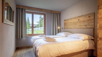 A bedroom with a bed, a window with curtains, a wooden headboard, and a view of trees outside.