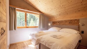 A wooden-paneled room with a bed, a window with curtains, and a wall-mounted light fixture.