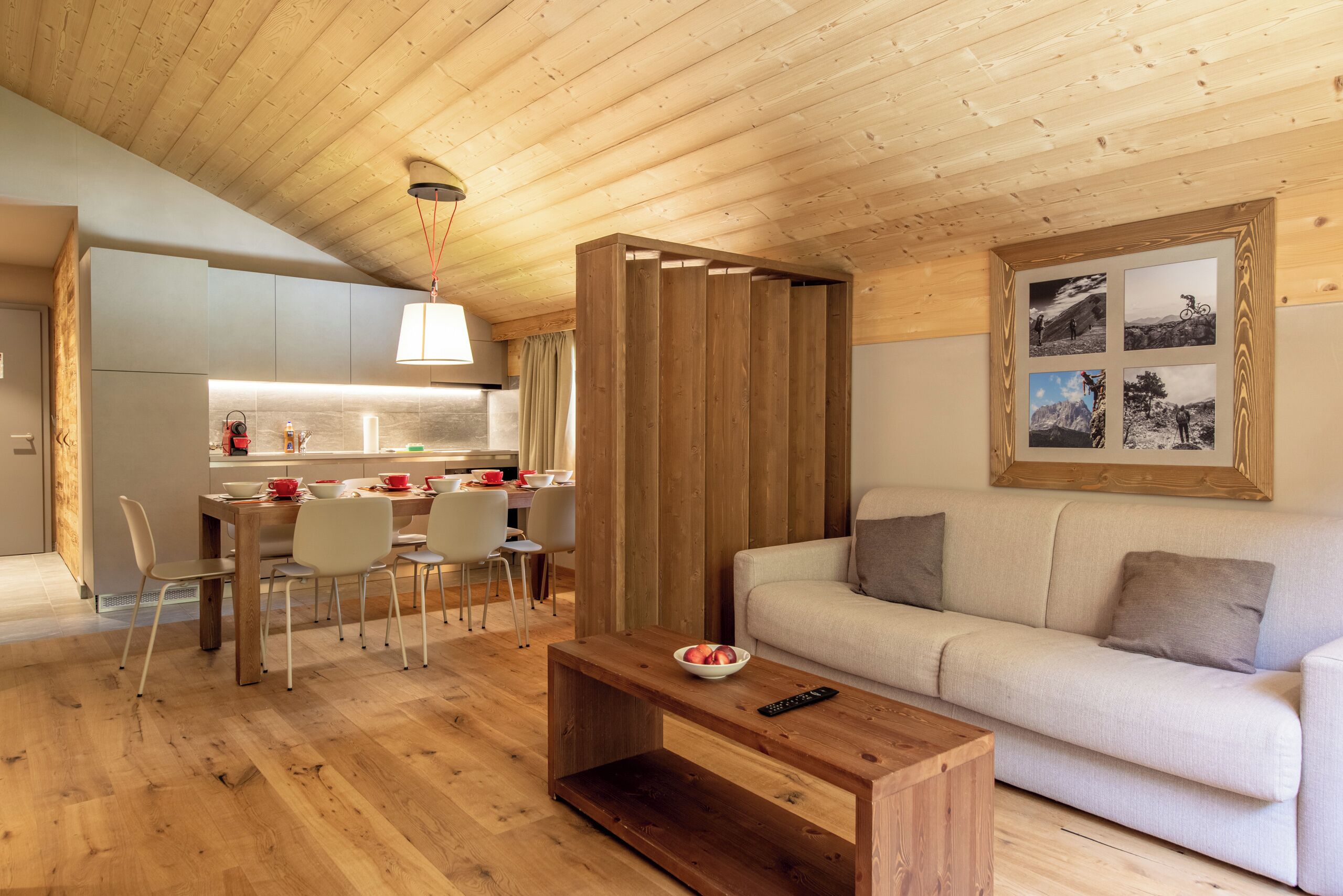 Et moderne interiør med træloft, spiseplads med stole og bord, en sofa og et billede i ramme på væggen.