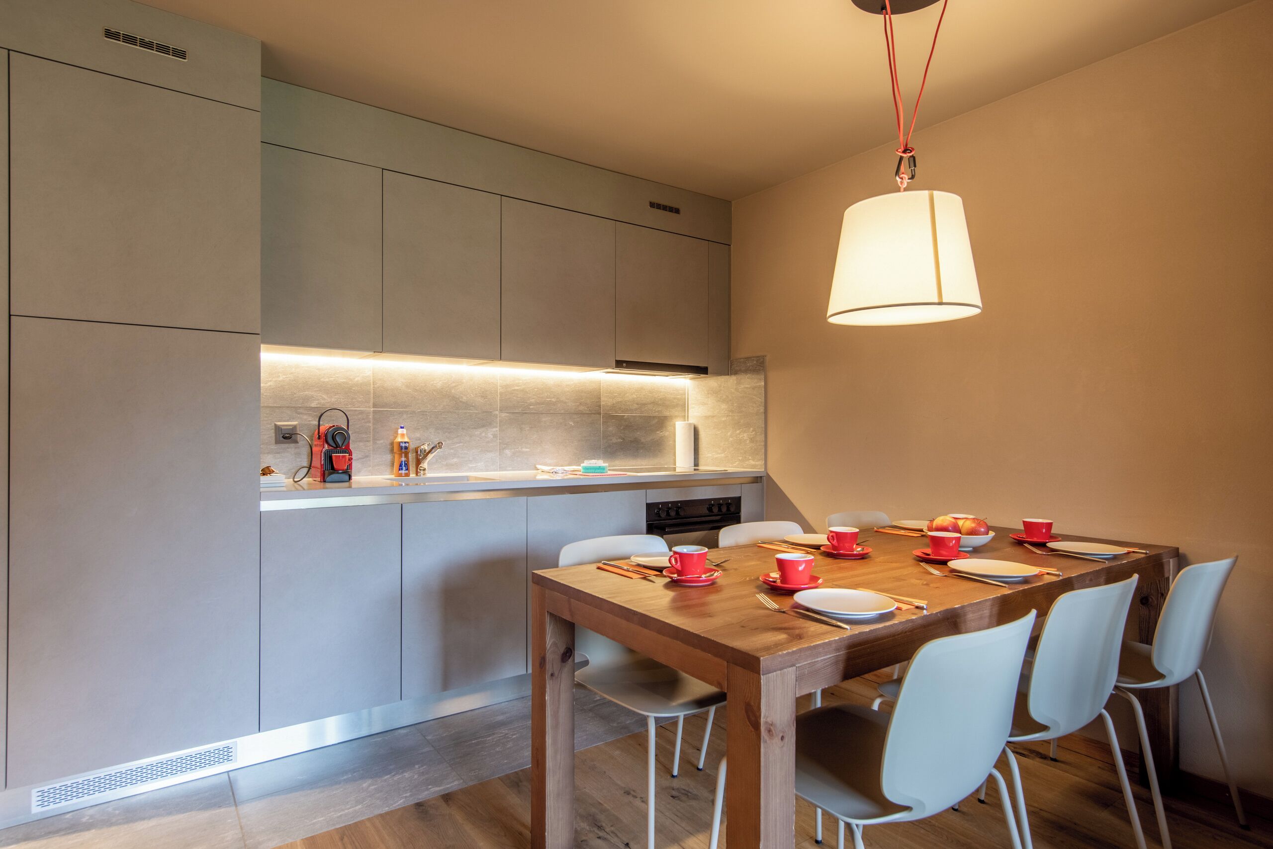 Eine moderne Küche mit Essbereich, darunter ein Holztisch und Stühle, eine Hängeleuchte und ein eingebauter Backofen.