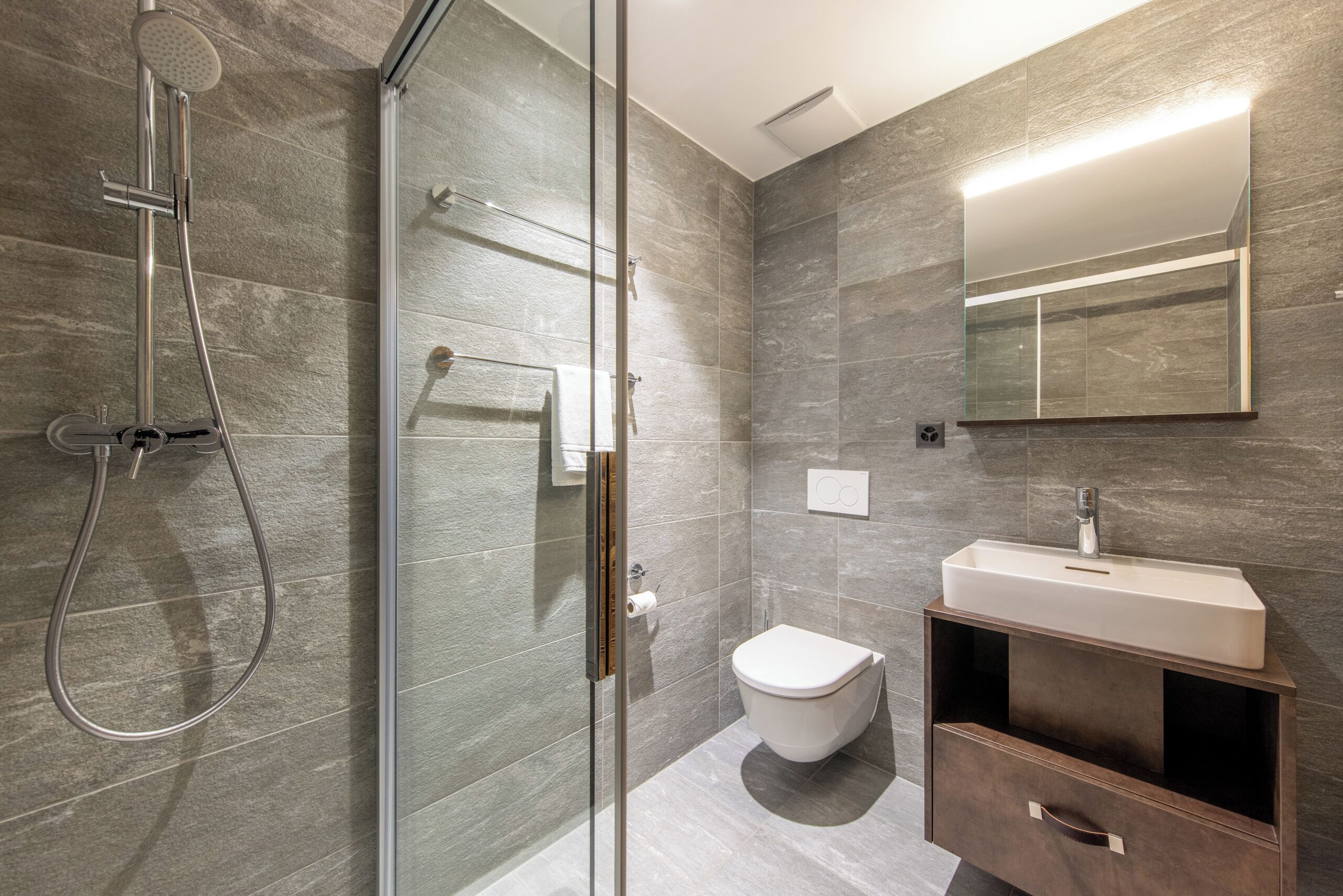 A modern bathroom with a glass shower enclosure, a white toilet, and a vanity with a mirror.