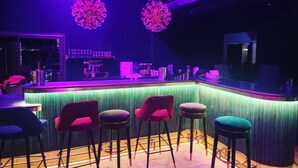 Zona de bar con una barra curva, varios taburetes y dos grandes lámparas decorativas.