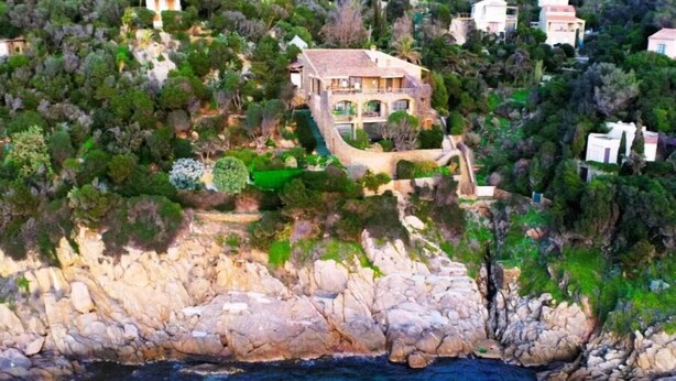 Una propiedad costera con una escalera de piedra que lleva a una casa rodeada de exuberante vegetación.