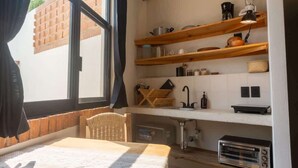 A compact kitchen with wooden shelves, a built-in oven, and a window with curtains. - Casa Aymara 601: Beach, Starlink & Privacy (Brisas de Zicatela)