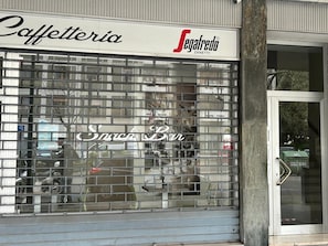 A storefront with a metal shutter, a sign reading "Caffetteria Segafredo Zanetti," and a reflection of a car and trees in the glass. - VENICE NIGHT13TRIPLA ROOM SHARED TOILETC (Mestre)