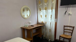 Habitación de hotel con cama, un escritorio de madera, una silla, televisión y ventana con cortina.
