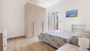 A bedroom with a bed, a nightstand, a lamp, a wardrobe, and a painting on the wall.