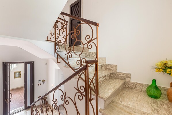 Una escalera con barandillas metálicas ornamentadas y un jarrón verde en el rellano.