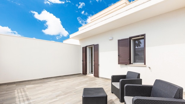 A rooftop terrace with a light-colored floor, two wicker sofas, and a small ottoman.