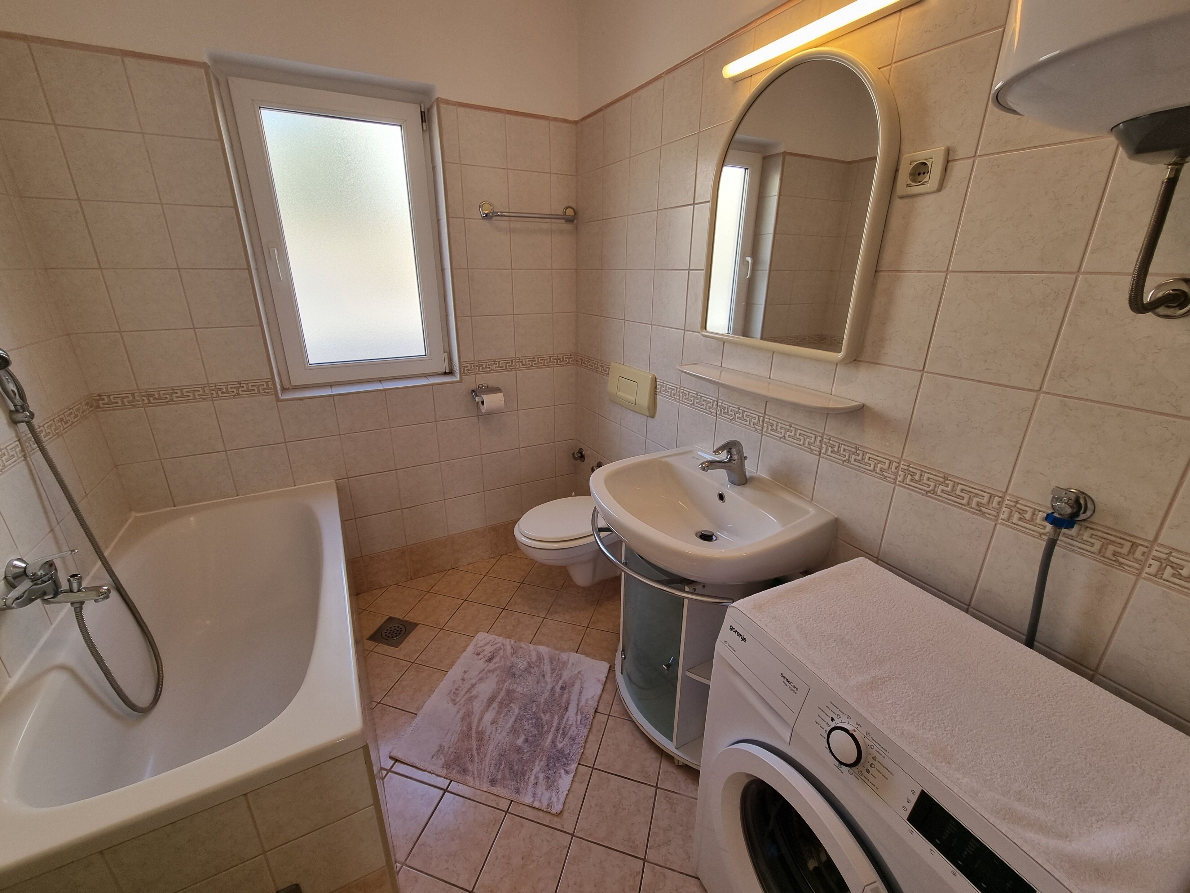 A bathroom with a bathtub, toilet, sink, and washing machine.