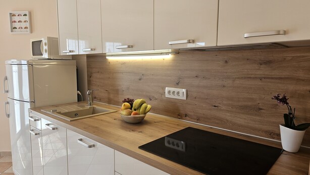 A modern kitchen with white cabinets, a wooden countertop, a black mat, and a bowl of fruit. - Nice apartment near beach and city ​​centre (Crikvenica)