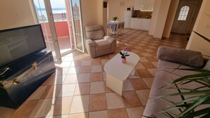 A living room with a sofa, a coffee table, and a TV on a cabinet. There is a sliding glass door leading to a balcony. - Nice apartment near beach and city ​​centre (Crikvenica)