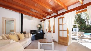 A living room with a sofa, a coffee table, and a TV. There is a window with curtains and a view of the outdoors.