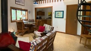 A spacious living area with a dining table, chairs, a sofa, a staircase, and a kitchen in the background. - Beaver Dome Geodesic Lake Home 3br 2bath (Rogers)