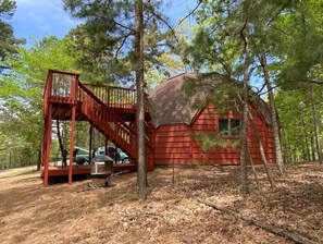 A red cabin with a wooden staircase leading to a deck, surrounded by trees. - Beaver Dome Geodesic Lake Home 3br 2bath (Rogers)