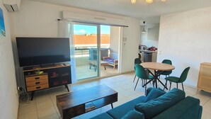 A living room with a TV, sofa, coffee table, and dining area with chairs and a table. - Appartement 2 Chambres, A 10 mn Plage et Commerces (Fréjus)