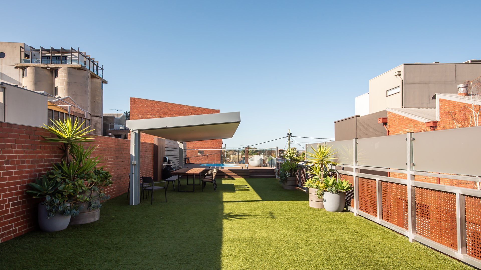 A modern outdoor patio area with artificial grass, a barbecue setup, and potted plants.