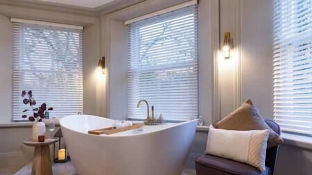 A modern bathroom with a freestanding bathtub, a wooden side table, and a chair with a cushion.