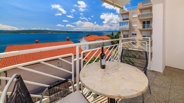 Ein Balkon mit Tisch und Stühlen mit Blick auf ein Gewässer und eine entfernte Küstenlinie.