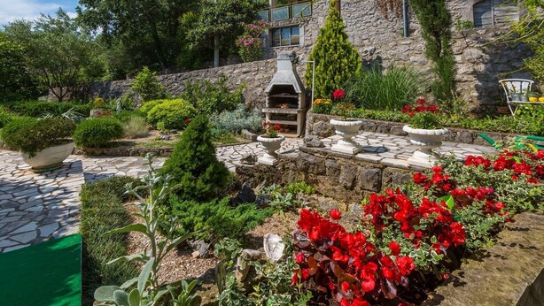 A stone patio with a barbecue area, surrounded by various plants and flowers. - Modern studio flat 500 metres to the beach (Dramalj)