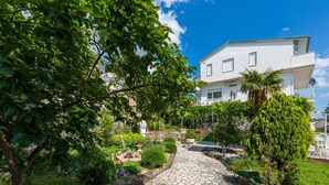 A stone pathway leading to a white building with a balcony, surrounded by lush greenery and a clear blue sky. - 500 metres to the beach with barbecue, air conditioning (Dramalj)