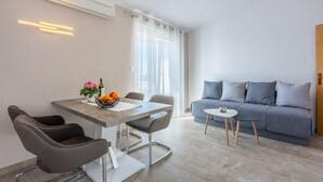 A modern living room with a grey sofa, a dining table with chairs, and a small side table. - 500 metres to the beach with barbecue, air conditioning (Dramalj)